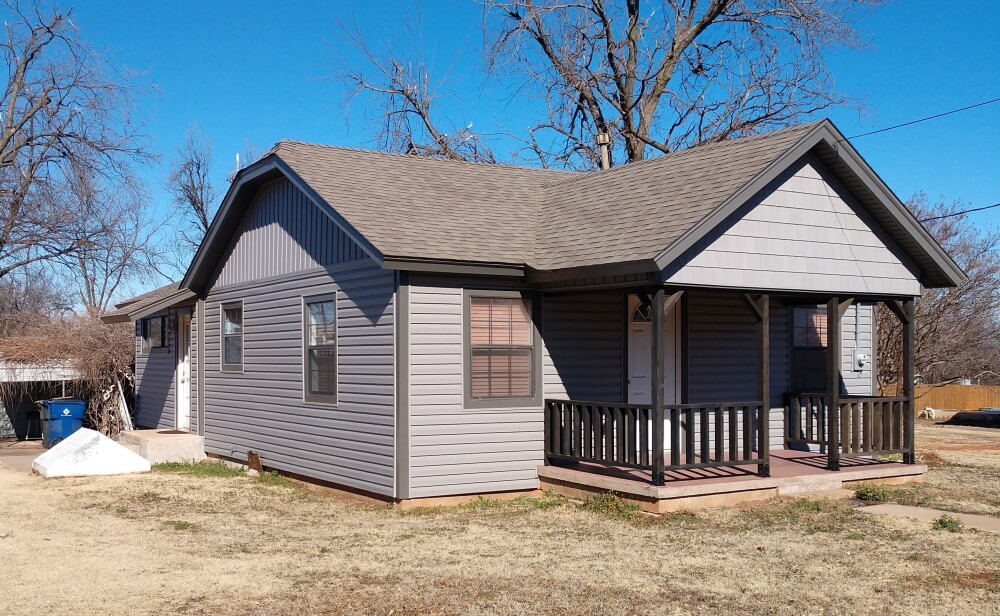 The Grey House rental — grey siding, covered front porch, under bare pecan trees