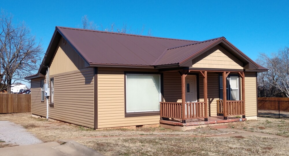 The Tan House rental — tan siding and a brown metal roof with a covered porch